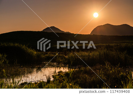 Summer 2024: Evening view around Okameike Pond in Soni Plateau. The sun sets over the mountains, painting the western sky golden. 117439408