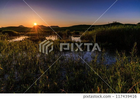 Evening scenery around Okameike Pond in the Soni Plateau in the summer of 2024. The sun sets behind the mountains, painting the western sky golden. Evening scenery around Okameike Pond in the Soni Plateau in the summer of 2024. The sun sets behind the mountains, painting the western sky golden. 117439416