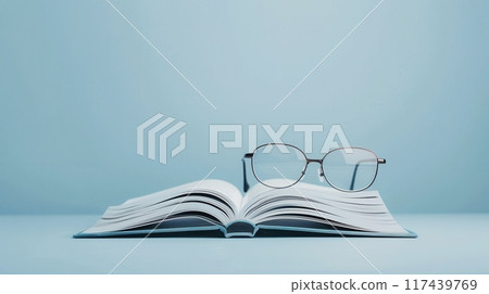 An open book with eyeglasses resting on top of it sits on a light blue background. 117439769