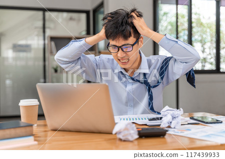 Frustrated and angry young businessman working late at the office trying to finish his project Frustrated and angry young businessman working late at the office trying to finish his project 117439933