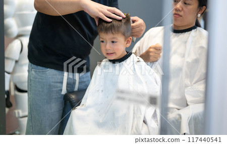 Young boy smiling during a haircut with caring barber in modern salon 117440541