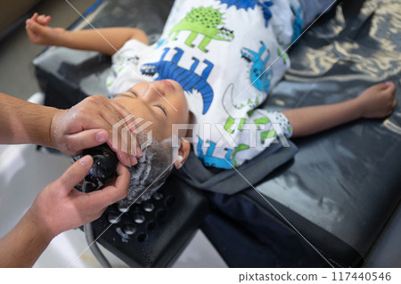 Child getting hair washed at a salon with a dinosaur-themed outfit on 117440546