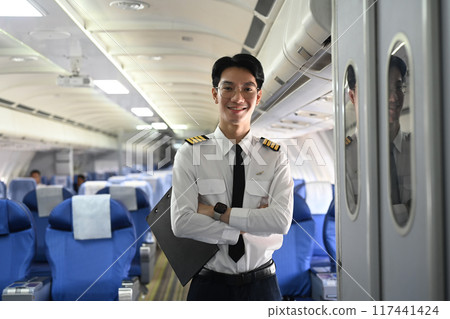 Portrait of smiling pilot standing with his arms crossed in the aisle of an airplane Portrait of smiling pilot standing with his arms crossed in the aisle of an airplane 117441424