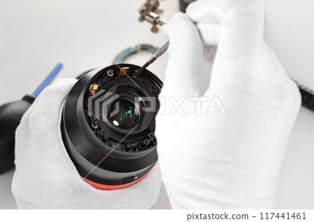 the hands of the master with gloves and a broken lens of a professional camera. 117441461