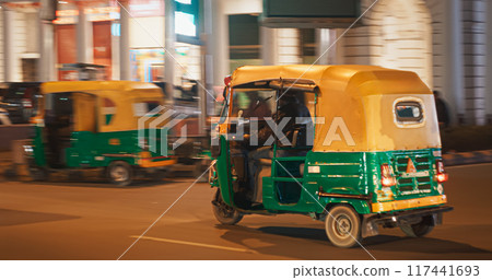 New Delhi, Delhi, India. Traffic On The Connaught Lane, Barakhamba street. Auto Rickshaw Or Tuk-tuk Moving On Street in night. Blurred motion. New Delhi, Delhi, India. Traffic On The Connaught Lane, Barakhamba street. Auto Rickshaw Or Tuk-tuk Moving On Street in night. Blurred motion. 117441693