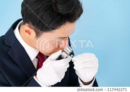 A man examining something with a magnifying glass 117442271