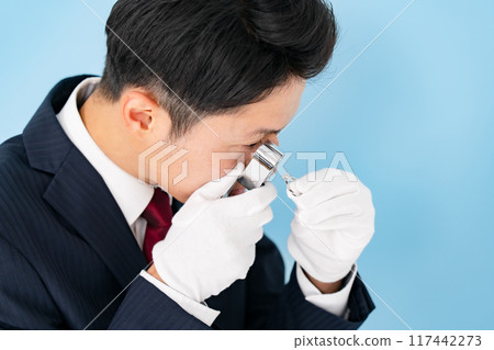 A man examining something with a magnifying glass 117442273