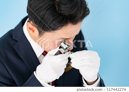 A man examining something with a magnifying glass 117442274