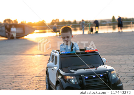 A little caucasian toddler boy of three and a half years old rides a toy car in a summer park near lake on a sunset light. Childhood and pastime A little caucasian toddler boy of three and a half years old rides a toy car in a summer park near lake on a sunset light. Childhood and pastime 117443273