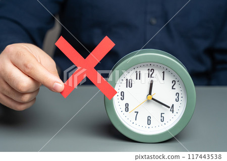 A man is holding a red no prohibition sign near clock. Prohibition of time change. Summer and winter time. Review laws, regulations 117443538