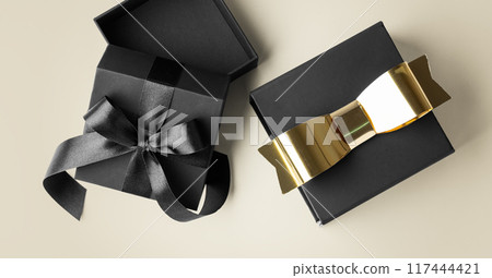 Opened black gift box and present with gold bow on light gold background Opened black gift box and present with gold bow on light gold background 117444421