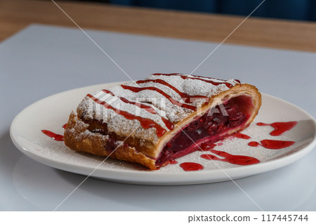 Dessert strudel with cherry and ice cream on a white plate 117445744