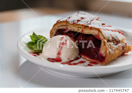 Dessert strudel with cherry and ice cream on a white plate 117445747
