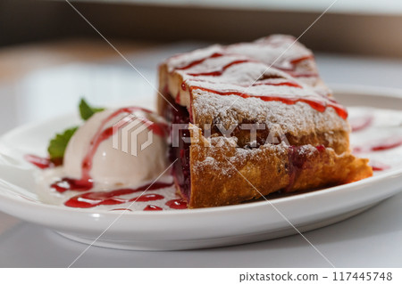 Dessert strudel with cherry and ice cream on a white plate Dessert strudel with cherry and ice cream on a white plate 117445748