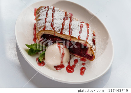 Dessert strudel with cherry and ice cream on a white plate Dessert strudel with cherry and ice cream on a white plate 117445749