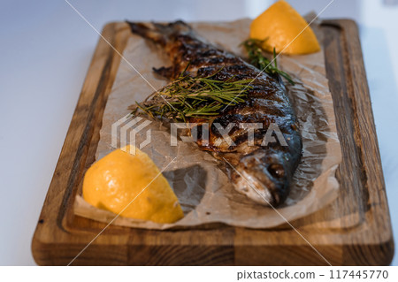 Dorado fish baked with lemon on a barbecue on a wooden board 117445770
