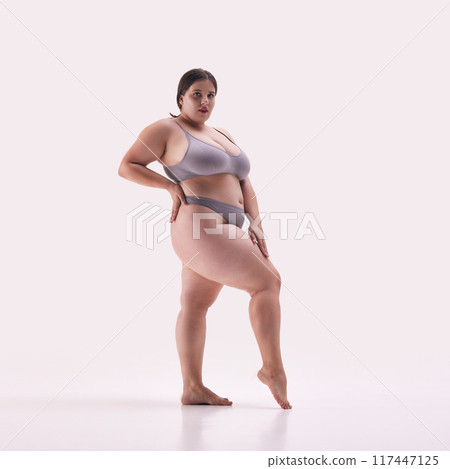 Curvy woman in grey underwear, exuding confidence and self-love against white studio background. Model plus size posing. 117447125