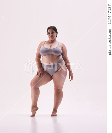 Empowered, beautiful plus size woman wearing grey underwear, standing strong and proud against white studio background. 117447127