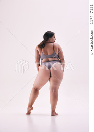Rear view photo of beautiful, young lady, model size plus posing in grey underwear exudes confidence against white studio background. Rear view photo of beautiful, young lady, model size plus posing in grey underwear exudes confidence against white studio background. 117447131