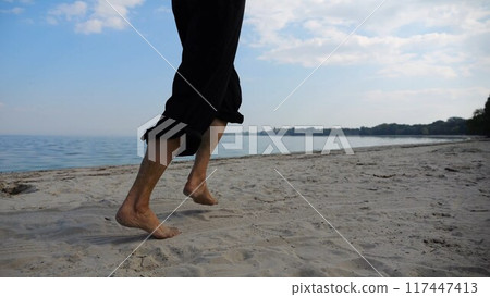 Bare feet of adult woman jogging on sand at the beach with seascape at background. Female legs running along sea shore. Happy lady spending time near ocean coast. Concept of summer vacation Bare feet of adult woman jogging on sand at the beach with seascape at background. Female legs running along sea shore. Happy lady spending time near ocean coast. Concept of summer vacation 117447413