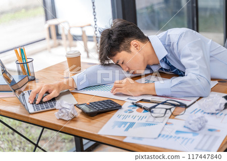 Tired and overworked young businessman falling to sleep while working late in his office 117447840