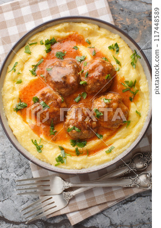 Creamy Polenta and Meatballs with gravy closeup on the bowl. Vertical top view Creamy Polenta and Meatballs with gravy closeup on the bowl. Vertical top view 117448589