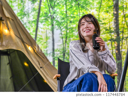 A young woman smiling with a beer in hand at glamping camp 117448784