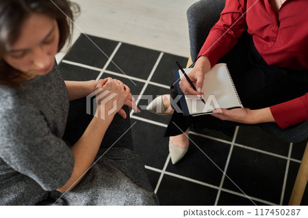 Two women having an informal discussion while one takes notes on a notebook on a patterned floor 117450287