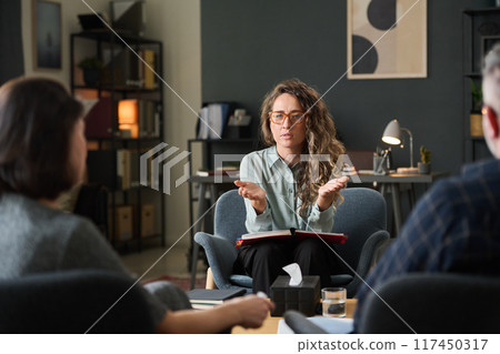 Three colleagues engaging in discussion about work strategies in a modern office setting, collaborating for project advancement and sharing ideas, seated around the table, Caucasian woman talking Three colleagues engaging in discussion about work strategies in a modern office setting, collaborating for project advancement and sharing ideas, seated around the table, Caucasian woman talking 117450317