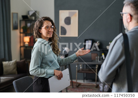 Business professional engaging in conversation while holding documents in modern office with a serene ambiance filled with decor and art on wall Business professional engaging in conversation while holding documents in modern office with a serene ambiance filled with decor and art on wall 117450350