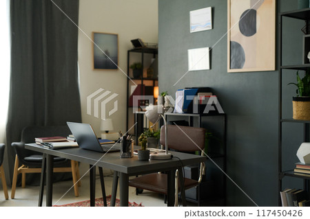 Home office setup with modern furnishings featuring sleek desk, organized bookshelves, and artistic wall decor on dark accent wall creating a serene workspace ambiance 117450426