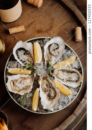Fresh oysters on ice served with lemon wedges and rosemary, perfect for gourmet seafood lovers 117450555