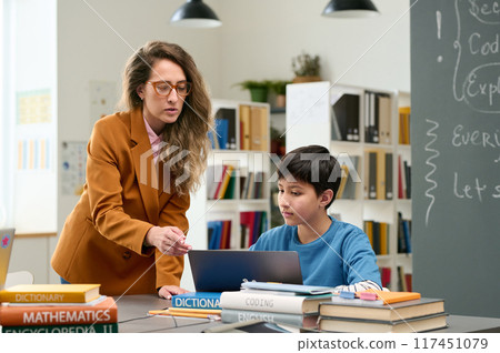 Portrait of young female teacher helping boy using laptop during computer class for children and pointing at screen copy space Portrait of young female teacher helping boy using laptop during computer class for children and pointing at screen copy space 117451079