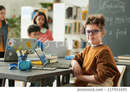 Portrait of funny young boy wearing glasses looking at camera in school library during computer class for children copy space 117451095