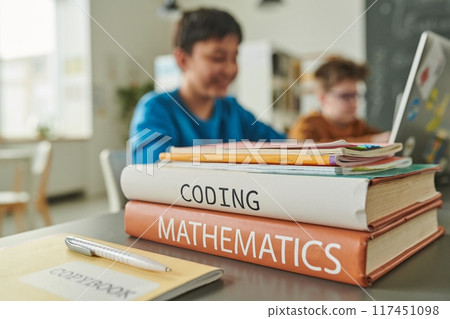 Close up of textbooks on coding and mathematics on table in school library with children in background copy space 117451098