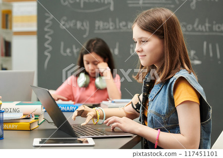 Side view portrait of smiling young girl with prosthetic arm using laptop during IT class for children in school copy space Side view portrait of smiling young girl with prosthetic arm using laptop during IT class for children in school copy space 117451101