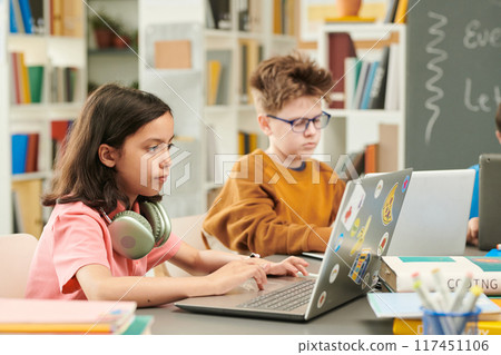 Side view portrait of young girl with big headphones using laptop during computer class for children copy space 117451106