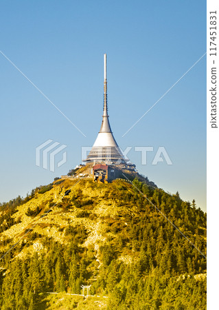 The Jested hotel majestically atop a verdant mountain, featuring a prominent TV transmitter. The clear sky highlights the unique architecture of the building surrounded by greenery. Liberec, Czechia 117451831
