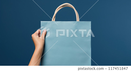 Shopping bag in woman's hand on blue background. Mockup design with blank space. Add text or logo. Generative Ai 117451847