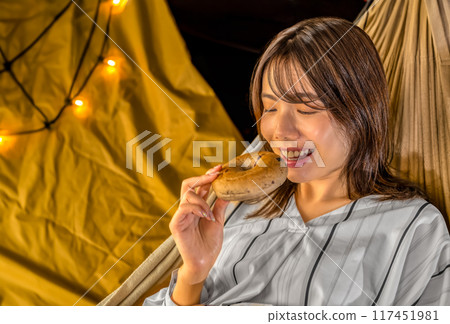 Young woman eating a bagel in a hammock while looking at the night sky Young woman eating a bagel in a hammock while looking at the night sky 117451981