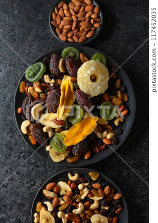 Dried tropical fruits, nuts, and raisins in black plate. 117452035