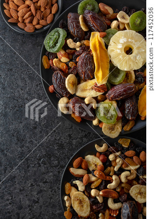 Dried tropical fruits, nuts, and raisins in black plate. 117452036