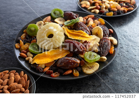 Dried tropical fruits, nuts, and raisins in black plate. 117452037