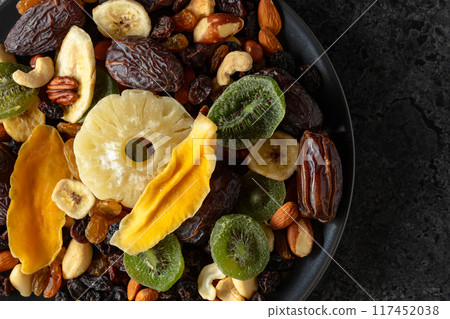 Dried tropical fruits, nuts, and raisins in black plate. 117452038