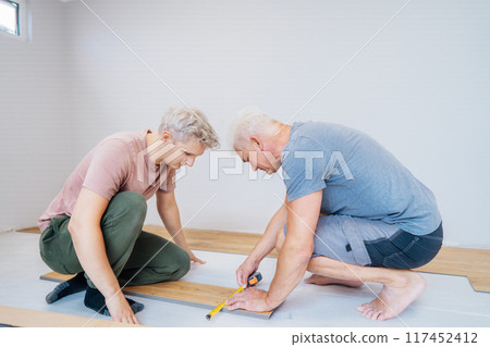 Father and adult son installing flooring in new Home by their own. Doing measurements, calculating for vinyl laminate and skirting. DIY, Do it yourself. Home renovation, improvement, refurbishment 117452412