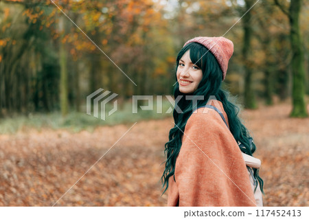 Woman in hat wrapped in warm Shawl Poncho enjoying autumn walk in forest with fall yellow leaves. Travel lifestyle. Feeling harmony, reunion with nature. Relaxing, personal fulfillment. Local travel Woman in hat wrapped in warm Shawl Poncho enjoying autumn walk in forest with fall yellow leaves. Travel lifestyle. Feeling harmony, reunion with nature. Relaxing, personal fulfillment. Local travel 117452413