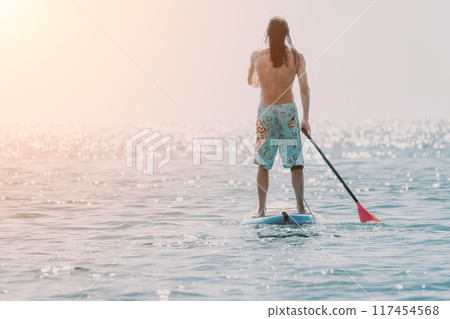 Man Sup Sea. Strong athletic man learns to paddle sup standing on board in open sea ocean on sunny day. Summer holiday vacation and travel concept. Aerial view. Slow motion 117454568