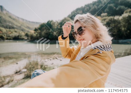Blonde Woman in Yellow Jacket Posing by a Lake Blonde Woman in Yellow Jacket Posing by a Lake 117454575