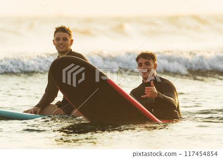 Smiling surfers sitting on their surfboards in the sea Smiling surfers sitting on their surfboards in the sea 117454854