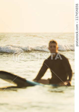 Out-of-focus surfer resting on his surfboard in the ocean Out-of-focus surfer resting on his surfboard in the ocean 117454856